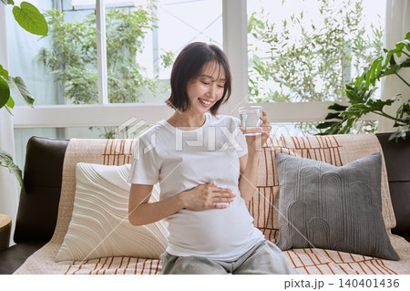 リビングのソファでコップの水を飲む笑顔の妊婦 リビングのソファでコップの水を飲む笑顔の妊婦 140401436