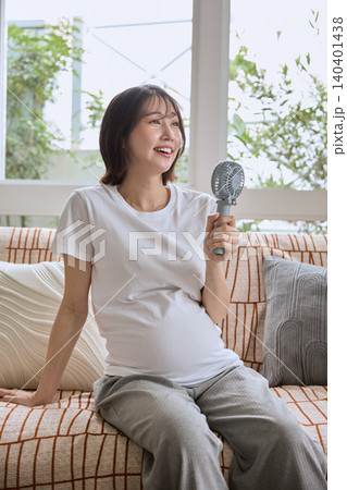 ソファに座りハンディファンで涼む若い妊婦 ソファに座りハンディファンで涼む若い妊婦 140401438