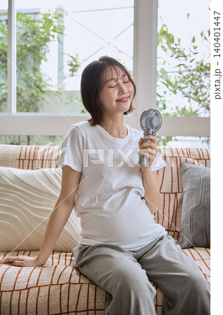 ソファでハンディファンを使って涼む若い女性 ソファでハンディファンを使って涼む若い女性 140401447
