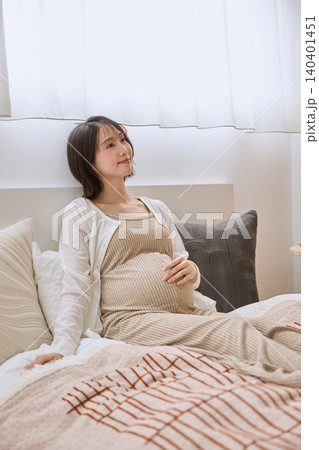 ベッドに座りお腹を押さえる若い妊婦 ベッドに座りお腹を押さえる若い妊婦 140401451