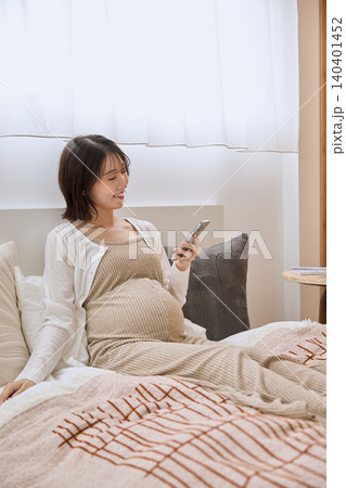 ベッドでスマートフォンを見て微笑む妊婦 ベッドでスマートフォンを見て微笑む妊婦 140401452