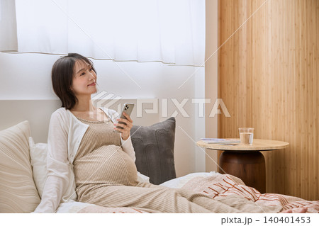 ベッドでスマートフォンを見て微笑む妊婦 ベッドでスマートフォンを見て微笑む妊婦 140401453