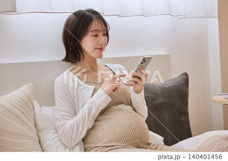 ベッドでスマートフォンを操作する妊婦 ベッドでスマートフォンを操作する妊婦 140401456