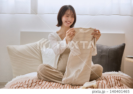 ベッドの上でベビー服を手に取り笑顔の若い女性 140401465