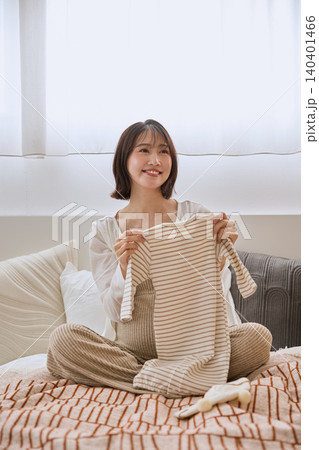 ベッドの上でベビー服を手に取り笑顔の若い女性 ベッドの上でベビー服を手に取り笑顔の若い女性 140401466