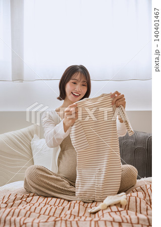 ベッドの上でベビー服を手に取り笑顔の若い女性 ベッドの上でベビー服を手に取り笑顔の若い女性 140401467