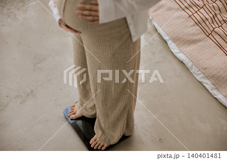 体重計に乗って腹部に手を当てる妊婦の足元 140401481