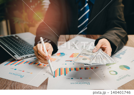 Businessman Analyzing Financial Data with Graphs, Cash, and Laptop in Modern Office Environment, Business concept 140401746