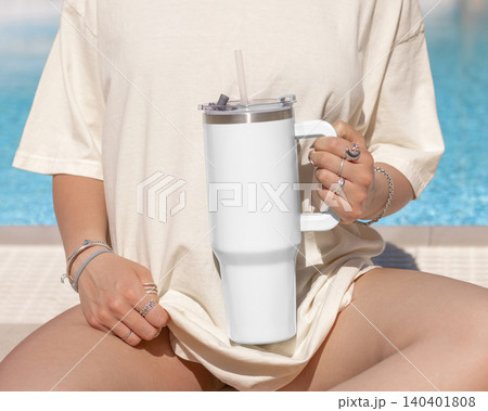 Blank white 40oz tumbler mockup, young woman at poolside, hand close up. Lifestyle scene Blank white 40oz tumbler mockup, young woman at poolside, hand close up. Lifestyle scene 140401808