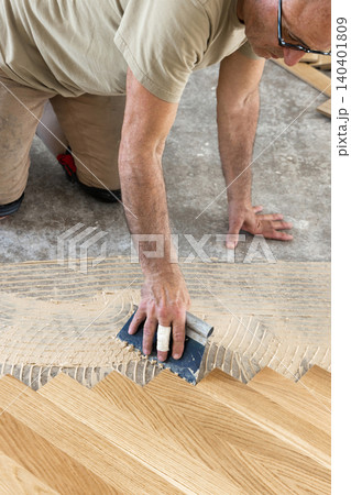 Worker applying parquet flooring adhesive with notched trowel during home construction, top view 140401809
