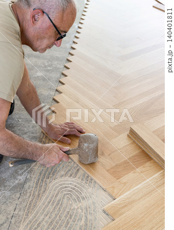 Worker installing herringbone parquet flooring with rubber mallet during hardwood floor installation 140401811