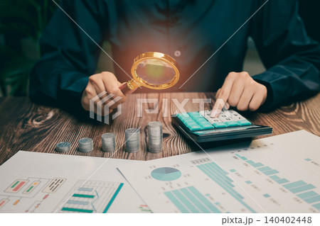 Detailed Financial Analysis with Calculator, Coins, and Magnifying Glass on a Wooden Table, Business concept Detailed Financial Analysis with Calculator, Coins, and Magnifying Glass on a Wooden Table, Business concept 140402448