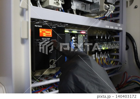 産業用制御キャビネット内のキーエンスPLCモジュールを点検するエンジニアの手 140403172