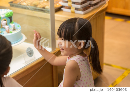 Excited little Asian girl looking at beautiful cake through glass display in a bakery shop, childhood birthday wishes. Excited little Asian girl looking at beautiful cake through glass display in a bakery shop, childhood birthday wishes. 140403608