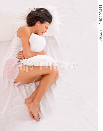 Woman, sad and stomach pain in bed with PMS, cramps and frustrated in bedroom or at home. Young person with pillow, crying and stress from above with endometriosis, uterus and gut or health risk Woman, sad and stomach pain in bed with PMS, cramps and frustrated in bedroom or at home. Young person with pillow, crying and stress from above with endometriosis, uterus and gut or health risk 140403841