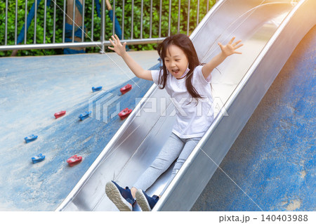 a cheerful girl sliding down a steel slide in the playground with open arms. a cheerful girl sliding down a steel slide in the playground with open arms. 140403988