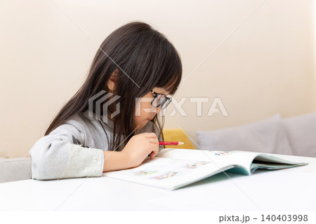 Diligent primary school girl writing in a notebook at her study desk at home. Diligent primary school girl writing in a notebook at her study desk at home. 140403998
