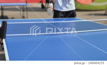 Adult playing table tennis outdoors, holding paddle hitting ping pong ball over net Adult playing table tennis outdoors, holding paddle hitting ping pong ball over net 140404255