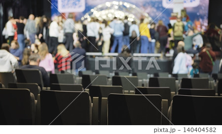 Empty audience seats in venue with blurred bustling crowd on stage 140404582