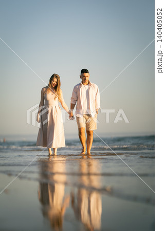 Couple walks on the beach holding hands during sunset near the ocean with footprints in the sand Couple walks on the beach holding hands during sunset near the ocean with footprints in the sand 140405052