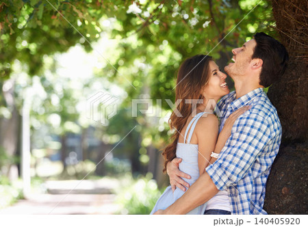 Young couple, laughing and hug with love under the trees in the park and enjoying sunshine views in the summer sun. Cheerful, affection outdoor and romantic partners bonding with a nature lifestyle 140405920