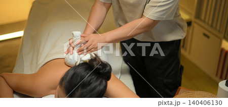 Relaxed woman receiving traditional herbal compress massage in a serene spa 140406130