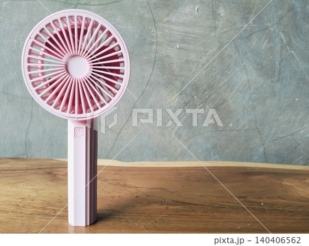 Compact Mini Electric Fan for Personal Cooling on a wooden table Compact Mini Electric Fan for Personal Cooling on a wooden table 140406562