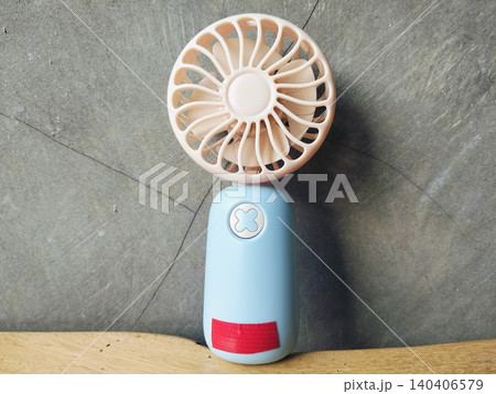 Compact Mini Electric Fan for Personal Cooling on a wooden table Compact Mini Electric Fan for Personal Cooling on a wooden table 140406579