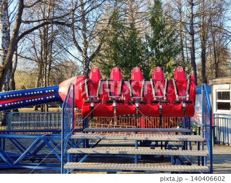 Row of empty red amusement park ride chairs on a sunny day 140406602