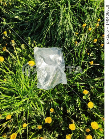 Plastic bag on lush green grass surrounded by yellow dandelions in a sunny park Plastic bag on lush green grass surrounded by yellow dandelions in a sunny park 140406619