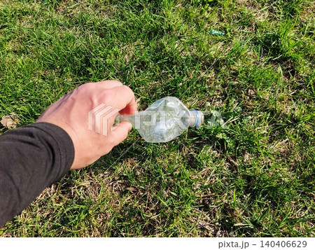 Hand picking up plastic bottle from grass to promote environmental responsibility Hand picking up plastic bottle from grass to promote environmental responsibility 140406629