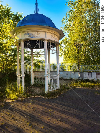 Tranquil white gazebo in lush green park with pathway and blue sky backdrop 140406698