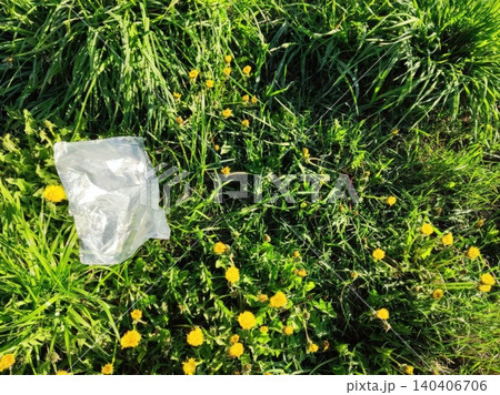 Plastic bag littering lush green grass among yellow dandelions in a natural setting Plastic bag littering lush green grass among yellow dandelions in a natural setting 140406706