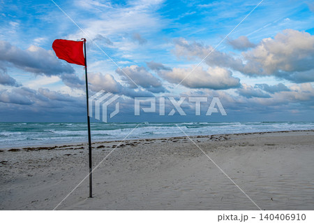 Red warning flag standing tall on a beach with cloudy skies and waves Red warning flag standing tall on a beach with cloudy skies and waves 140406910
