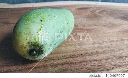 Single raw organic green mango placed on a wood surface. Single raw organic green mango placed on a wood surface. 140407007