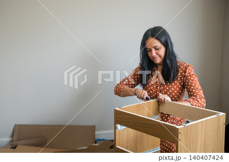 A woman is working on a wooden box, possibly assembling it A woman is working on a wooden box, possibly assembling it 140407424