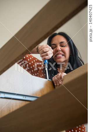 A woman is using a screwdriver to fix a piece of furniture A woman is using a screwdriver to fix a piece of furniture 140407425