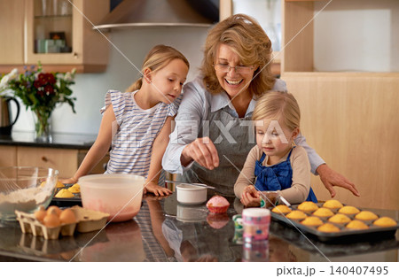 Grandma, kid and baking with teaching, smile and decorating for cheerful bonding together at home. Happy, pensioner or girl child with cupcake, laugh or icing for creative, playful or fun in kitchen 140407495