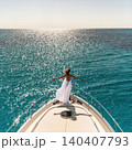 Young woman in white dress standing on yacht bow over turquoise sea 140407793