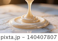 Thick white condensed milk pouring smoothly onto marble surface in warm light 140407807