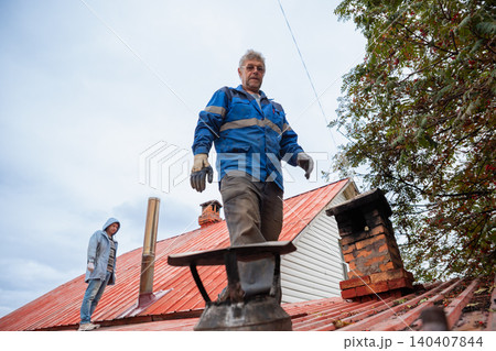 Chimney sweep working on house roof. Professional man repairing building ventilation system. Maintenance service for heater and fireplace. Construction worker fixing roof chimney exterior. Chimney sweep working on house roof. Professional man repairing building ventilation system. Maintenance service for heater and fireplace. Construction worker fixing roof chimney exterior. 140407844