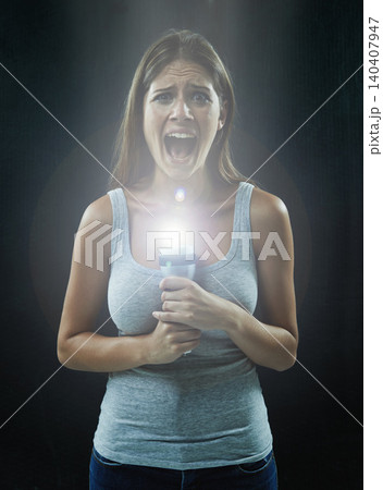 Woman, portrait and scared or flashlight for scream in studio, anxiety and stress for risk in mystery. Female person, shout and lamp in dark against black background, caution and danger or horror 140407947