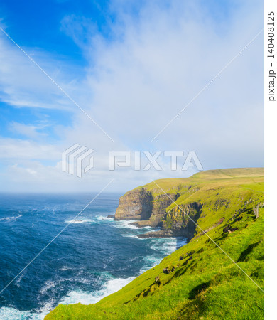 Scenic summer landscape of Faroe Islands with green fields, meadows and rocky cliffs by the ocean. 140408125