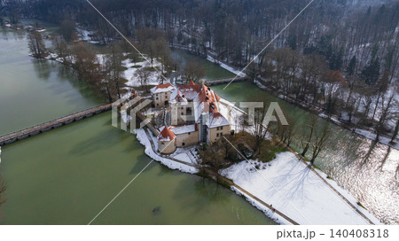 Picturesque drone panorama shows historic Otocec Castle covered in light snow. Frozen park trees, wooden bridges, and cold green Krka river frame medieval island palace in winter time. 140408318