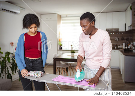 Mother ironing clothes while daughter is looking at her Mother ironing clothes while daughter is looking at her 140408524