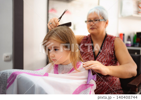 Hairdresser giving little girl haircut in beauty salon Hairdresser giving little girl haircut in beauty salon 140408744