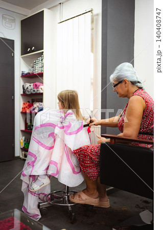 Hairdresser cutting little girl's long blond hair in salon Hairdresser cutting little girl's long blond hair in salon 140408747