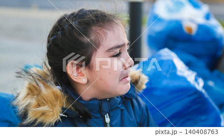 Little girl crying by blue garbage bags, showing distress and sadness Little girl crying by blue garbage bags, showing distress and sadness 140408763