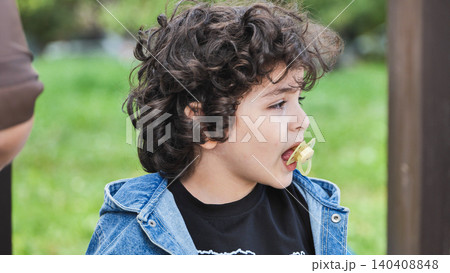 Curly haired child with pacifier outdoors, profile of a kid having a childhood moment Curly haired child with pacifier outdoors, profile of a kid having a childhood moment 140408848