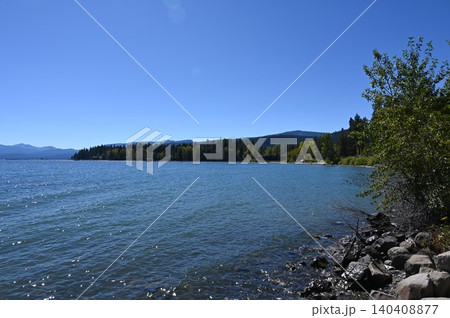 Rocky shoreline of a deep blue alpine lake with forested hills. Rocky shoreline of a deep blue alpine lake with forested hills. 140408877